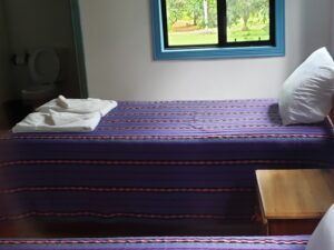 A bed with purple sheets and pillows in front of a window.